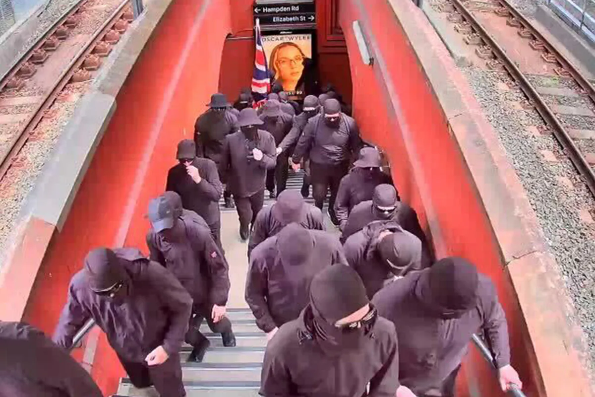 A supplied image shows a group of about 40 men seen wearing black balaclavas and brandishing Australian flags at Artarmon train station in Sydney, on Jan. 26, 2024. (AAP Image/Supplied by Transport for NSW)