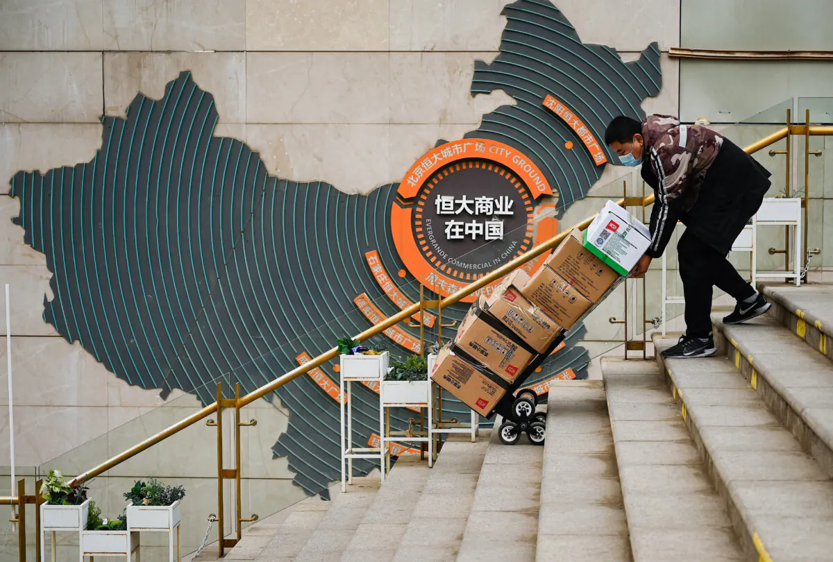 A worker pusher a cart in front of a sign showing Evergrande Group's China operation at a housing complex by the property developer in Beijing on Dec. 8, 2021. (Noel Celis/AFP via Getty Images)
