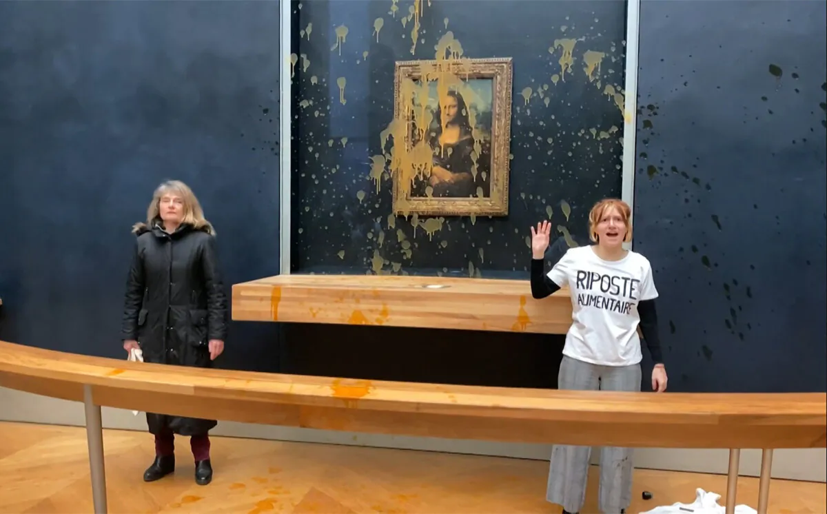 Two environmental activists from the collective dubbed "Riposte Alimentaire" (Food Retaliation) stand in front of Leonardo Da Vinci's "Mona Lisa" (La Joconde) painting after hurling soup at the artwork, at the Louvre museum in Paris, on Jan. 28, 2024. (David Cantiniaux/AFPTV/AFP via Getty Images)