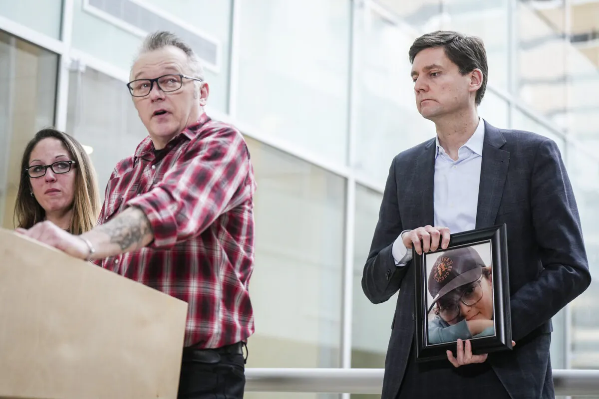Premier David Eby (R) holds a photograph of late 12-year-old Carson Cleland, who killed himself last year after becoming a victim of online sextortion, as his parents Ryan Cleland and Nicola Smith speak about him during a news conference in Surrey, B.C., on Jan. 26, 2024. (The Canadian Press/Darryl Dyck)