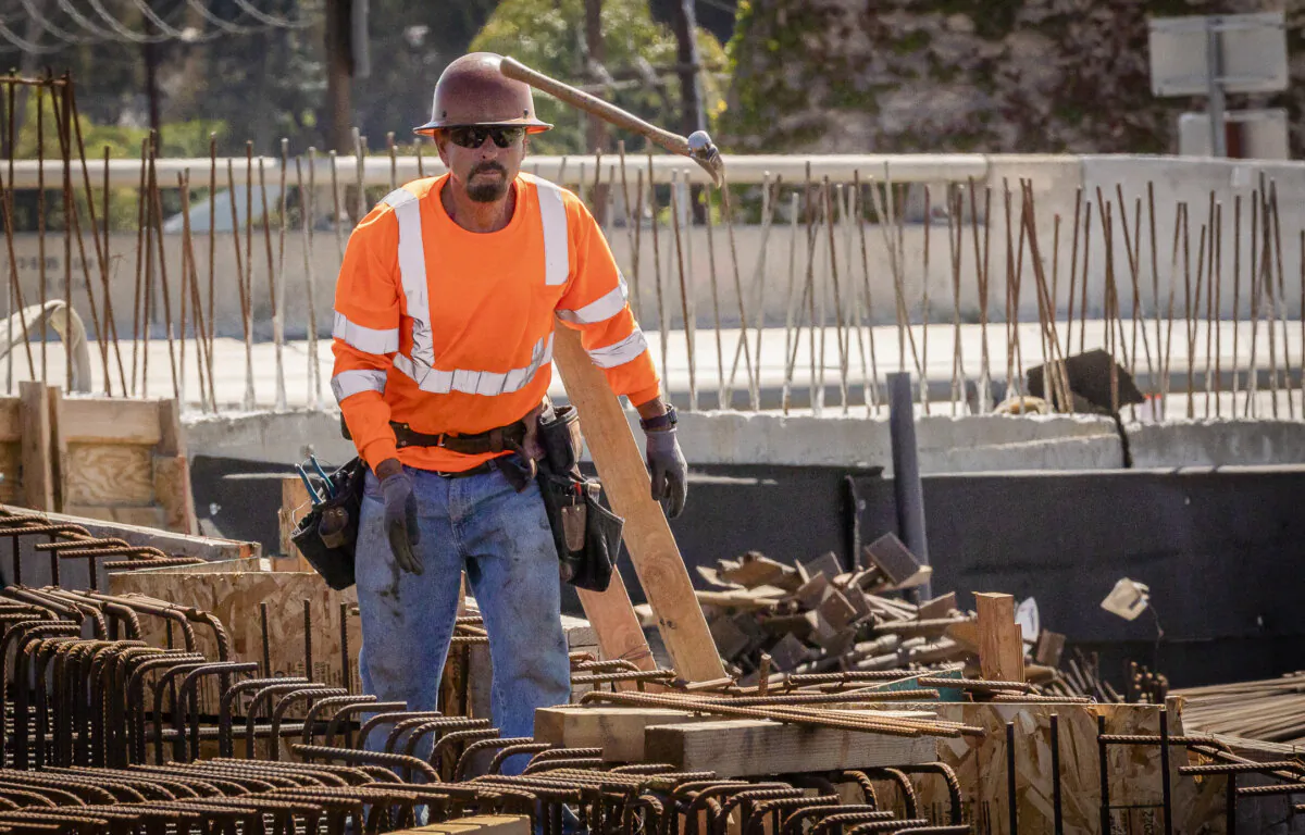 A worker tosses a hammer to a colleague  as construction continues on the HWY 73 southern interchange from the 405 freeway in Costa Mesa, Calif., on April 21, 2022. (John Fredricks/The Epoch Times)