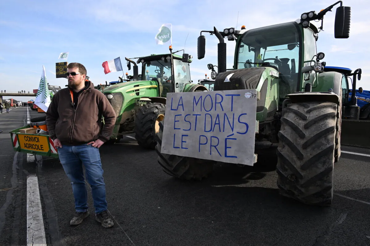 A French farmer takes part in a road block protest on the A4 highway next to a tractor with a placard reading "Death is in the field" near Jossigny, east of Paris, on Jan. 29, 2024, amid nationwide protests called by several farmers unions on pay, tax and regulations. (Bertrand Guay/AFP via Getty Images)