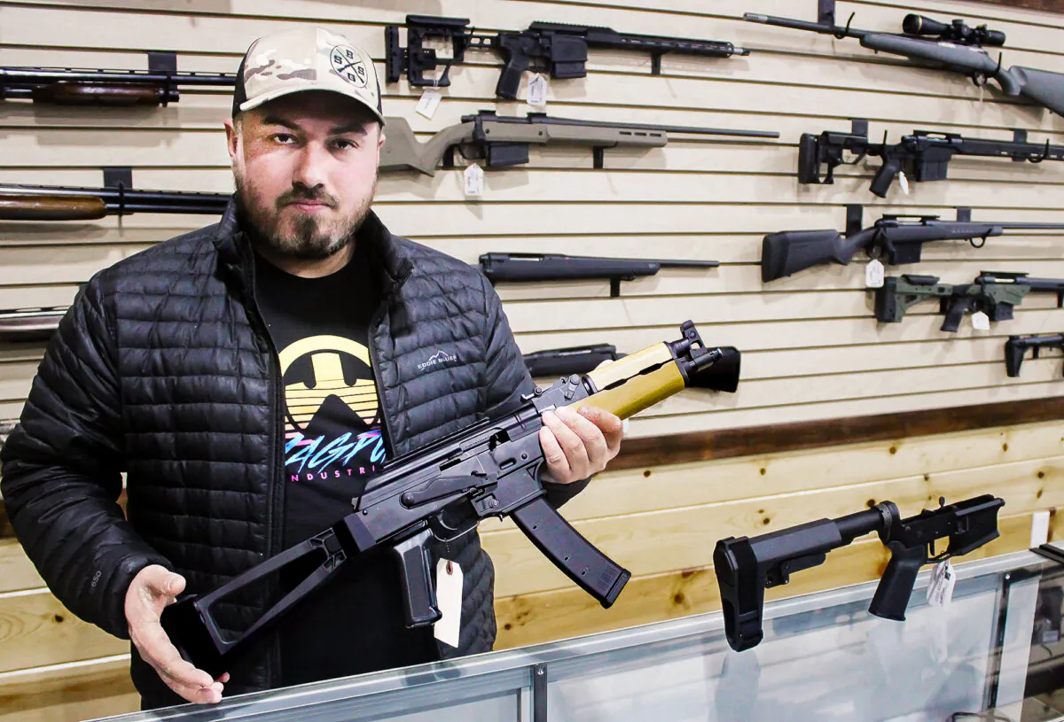 Justin Barrett, owner of Barrett Outdoors in Durant, Oklahoma, displays an AK pistol with a pistol stabilizing brace. On the counter next to him is a similar brace for an AR15 pistol. (Michael Clements/The Epoch Times)