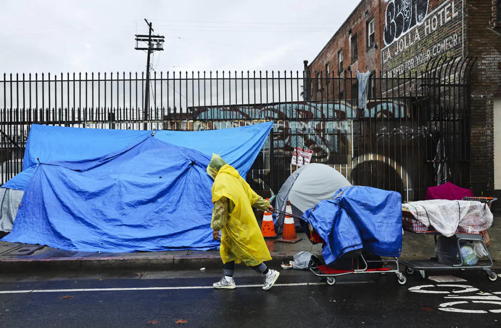 A person walks with carts in the rain near an encampment of unhoused people in Skid Row as a powerful long-duration atmospheric river storm, the second in less than a week, continues to impact Southern California in Los Angeles on Feb. 6, 2024. (Mario Tama/Getty Images)