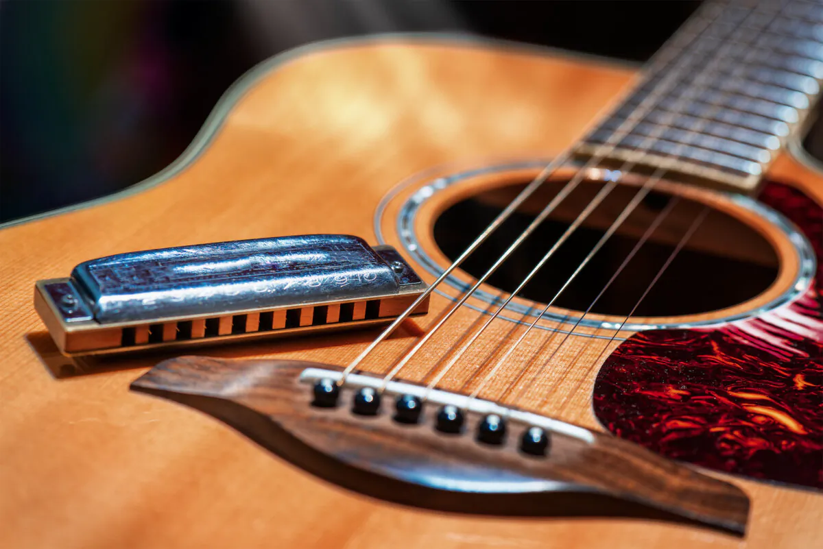 A acoustic guitar with country blues harmonica ready on stage. (Sutterstock)