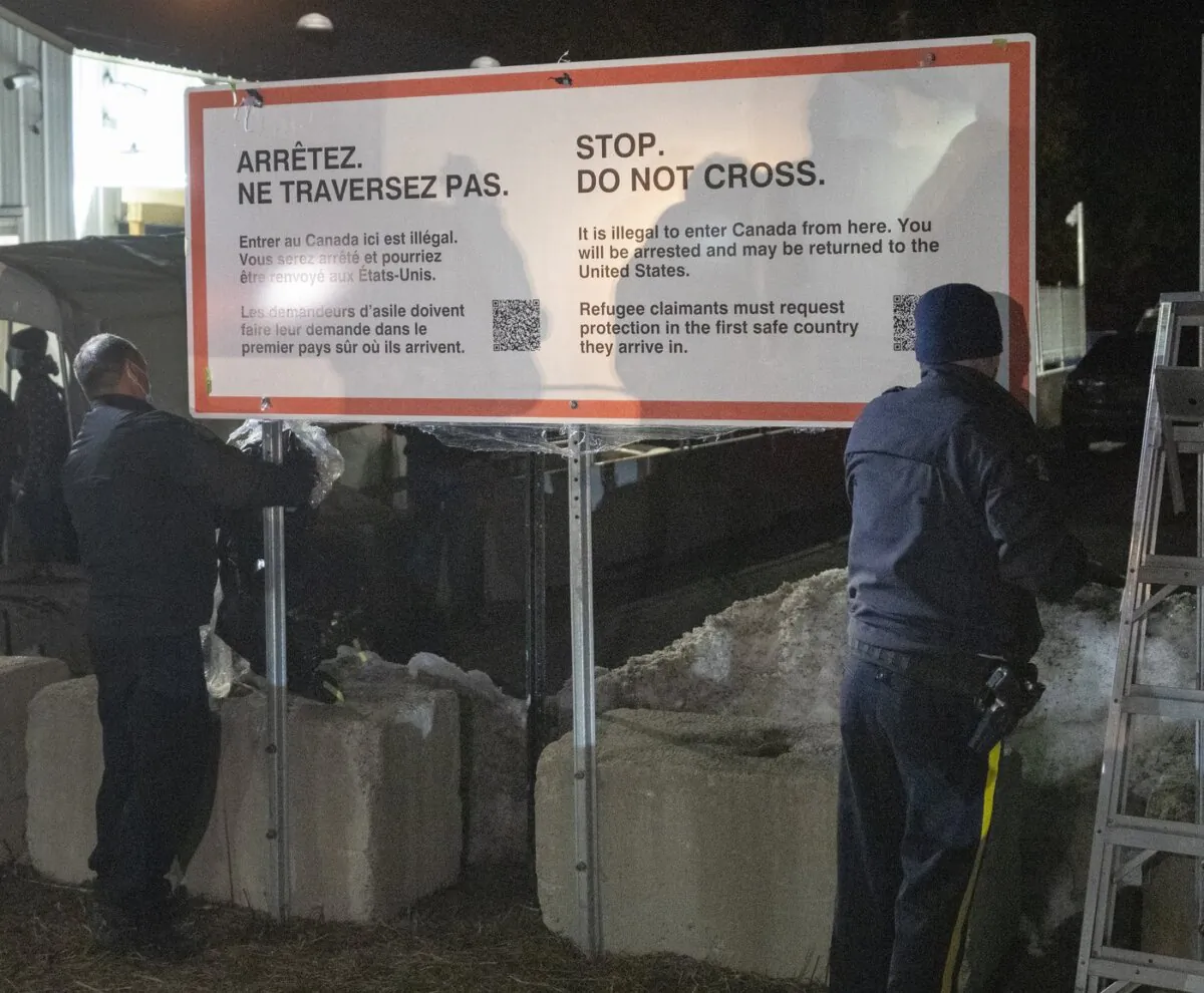 RCMP officers unwrap a new warning sign for asylum seekers on the border at Roxham Road from New York into Canada in Champlain, N.Y. on March 25, 2023. (The Canadian Press/Ryan Remiorz)