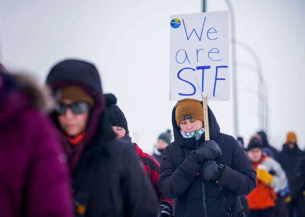 A woman holds a sign while walking at a demonstration site during a province-wide, one-day strike organized by the members of Saskatchewan Teachers’ Federation in Saskatoon Jan. 22, 2024. (The Canadian Press/Heywood Yu)
