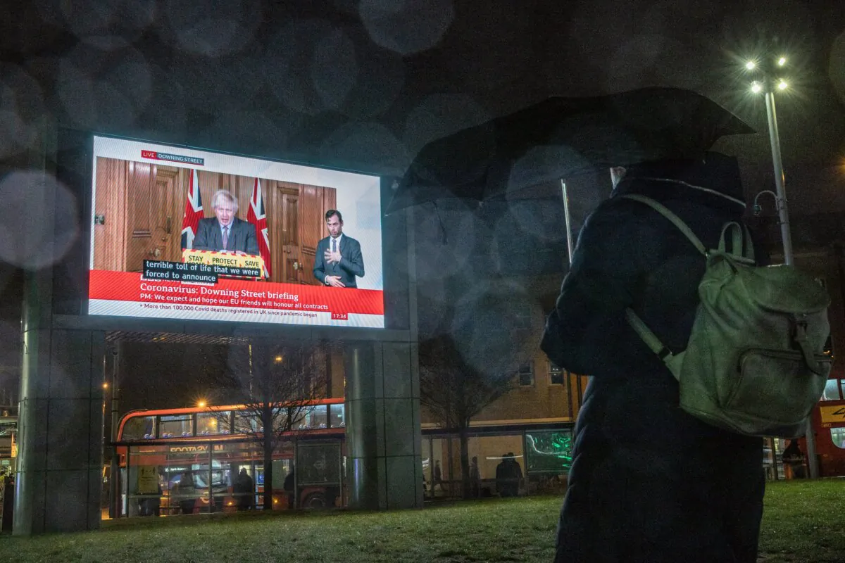 A woman watches the Downing Street briefing on a display board as it's announced that nearly 104,000 people have died from COVID-19, according to the Office for National Statistics, in London, on Jan. 26, 2021. (Dan Kitwood/Getty Images)