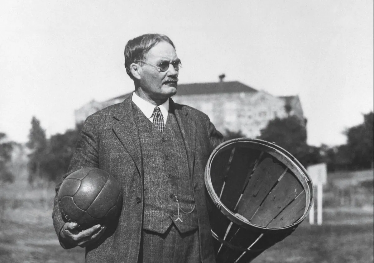 The inventor of basketball, James
Naismith, stands in a
field carrying a ball
and a peach basket,
circa early 1900s. (Public domain)