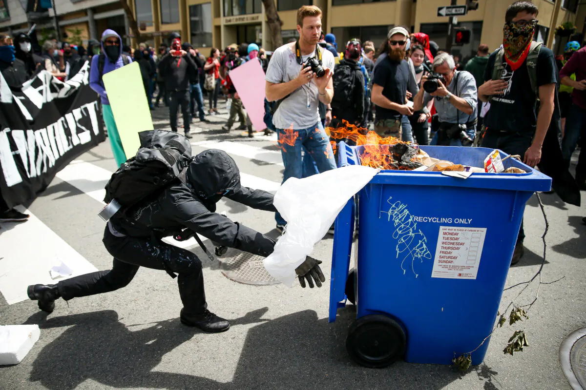 An Antifa extremist pushes a burning recycling bin toward Trump supporters during a free speech rally in Berkeley, Calif., on April 15, 2017. (Elijah Nouvelage/Getty Images)