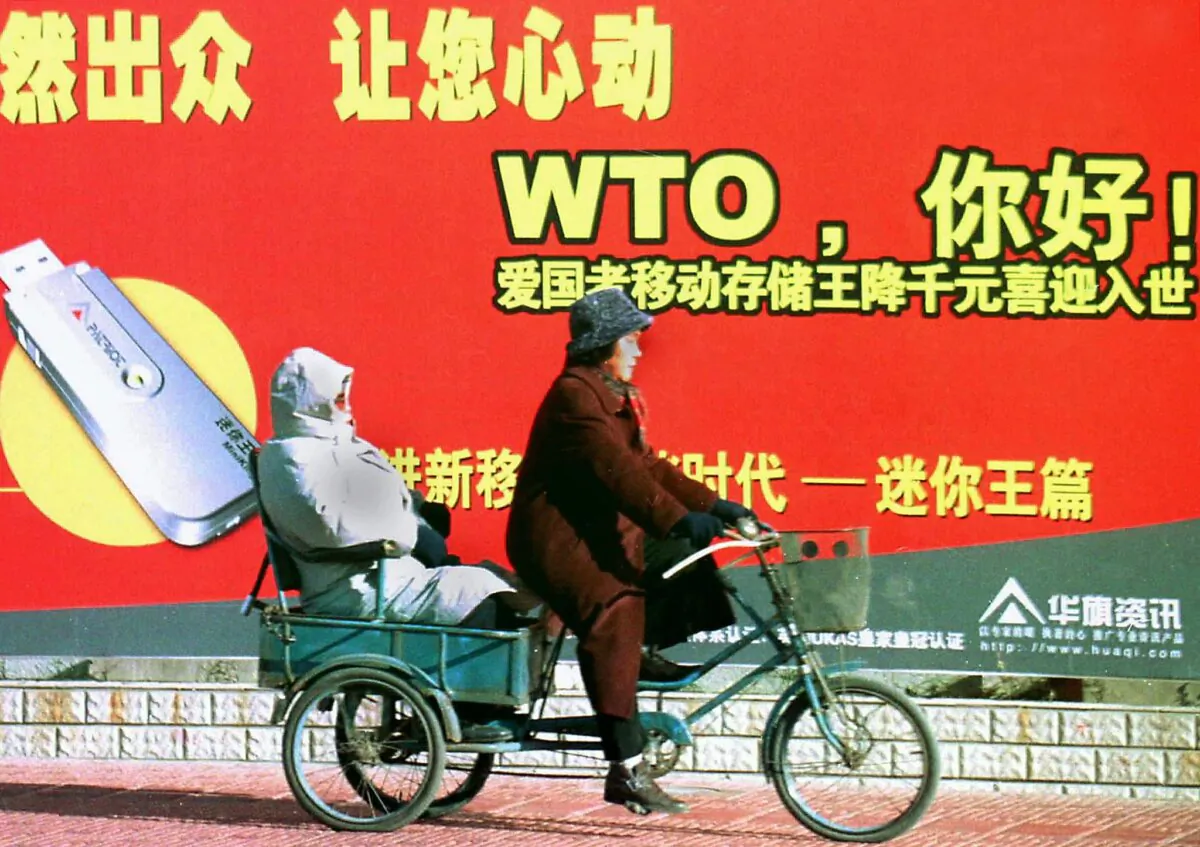 A Chinese couple on a tricycle pass a billboard welcoming the country's membership to the World Trade Organisation (WTO), along a street in Beijing on Dec. 23, 2001. (AFP via Getty Images)