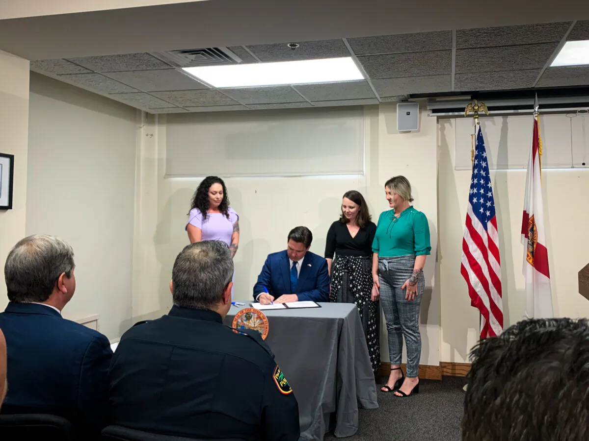 Victims of Jeffrey Epstein watch as Florida Gov. Ron DeSantis signs bill paving the way for the release of the 2006 grand jury testimony at a press conference in Palm Beach, Fla. on Feb. 29, 2024 (T.J. Muscaro/The Epoch Times).