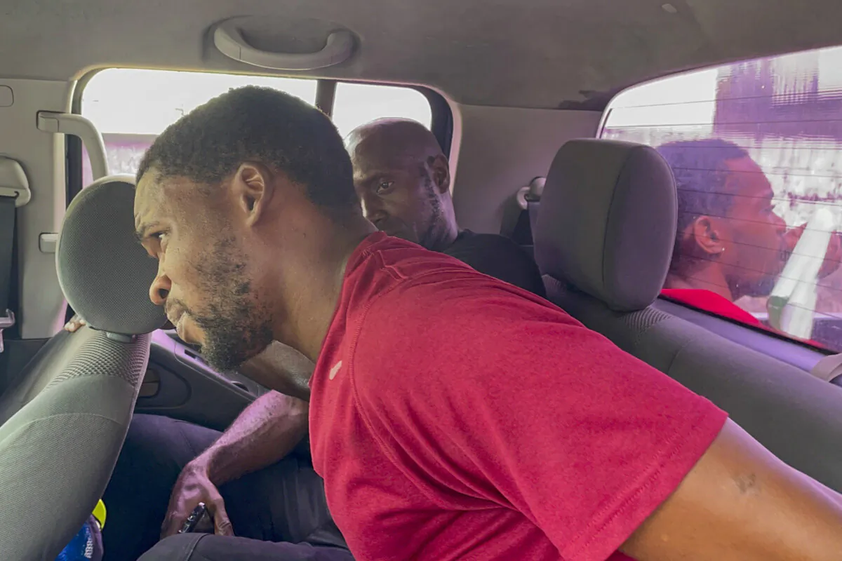 Escaped prisoner Ron Mitchell sits next to a police officer inside a police pickup as he waits to be taken back to prison, along with two other escapees, sitting in the truck bed, in Kingstown, St. Vincent and the Grenadines, on March 4, 2024. (Kenton Chance/AP Photo)