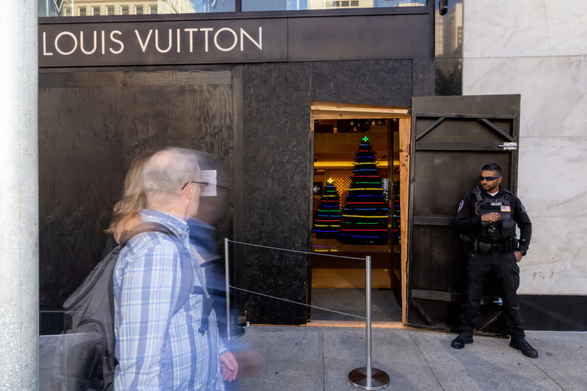 A security guard watches the entrance to a Louis Vuitton store, which has had its windows boarded near Union Square in San Francisco, Calif., on Nov. 30, 2021. Stores have increased security in response to a spike in thefts. (Ethan Swope/Getty Images)