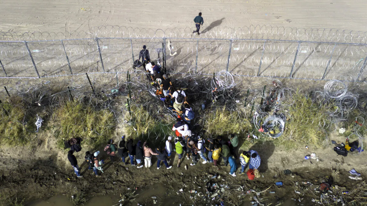 Illegal immigrants pass through coils of razor wire while crossing the U.S.–Mexico border in El Paso, Texas, on March 13, 2024. (John Moore/Getty Images)