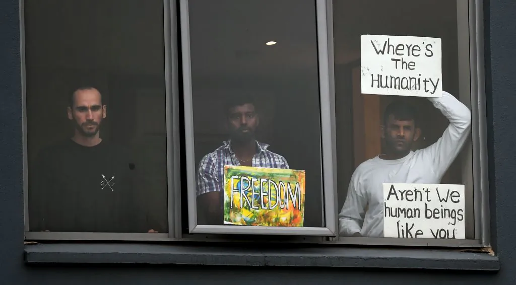 Three asylum seekers gesture to protesters holding a pro-refugee rights rally from their hotel room where they have been detained in Melbourne on June 13, 2020, after they were evacuated to Australia for medical reasons from offshore detention centres on Nauru and Manus Island. (Photo by William WEST / AFP) (Photo by WILLIAM WEST/AFP via Getty Images)