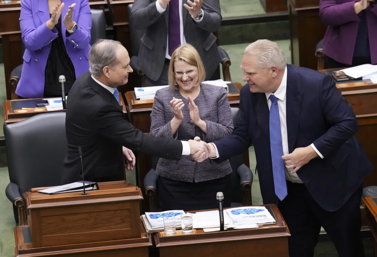 Finance Minister Peter Bethlenfalvy (L) shakes hands with Premier Doug Ford as Health Minister Sylvia Jones looks on, after Mr. Bethlenfalvy tabled the Ontario provincial budget at the legislature at Queen's Park in Toronto on March 26, 2024. (The Canadian Press/Nathan Denette)