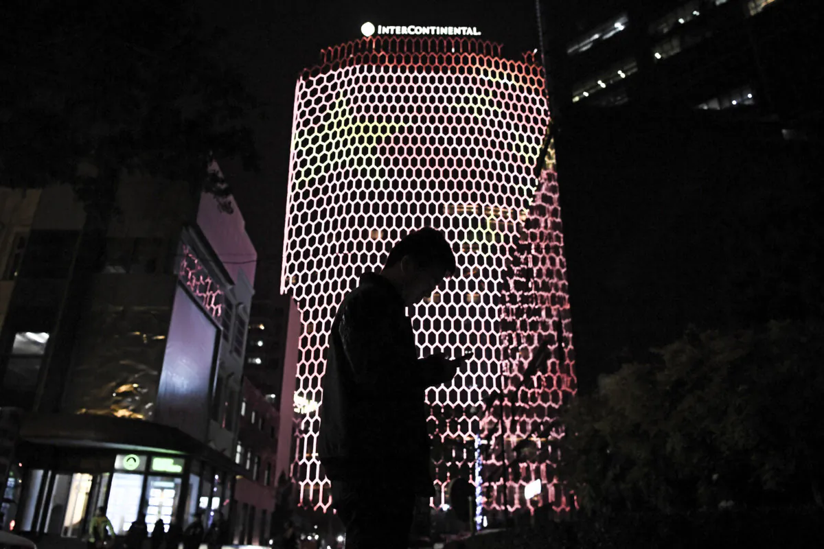 A man looks at his phone near a giant image of the CCP flag on the side of a building in Beijing, during the ongoing 19th Communist Party Congress, on Oct. 23, 2017. (GREG BAKER/AFP via Getty Images)