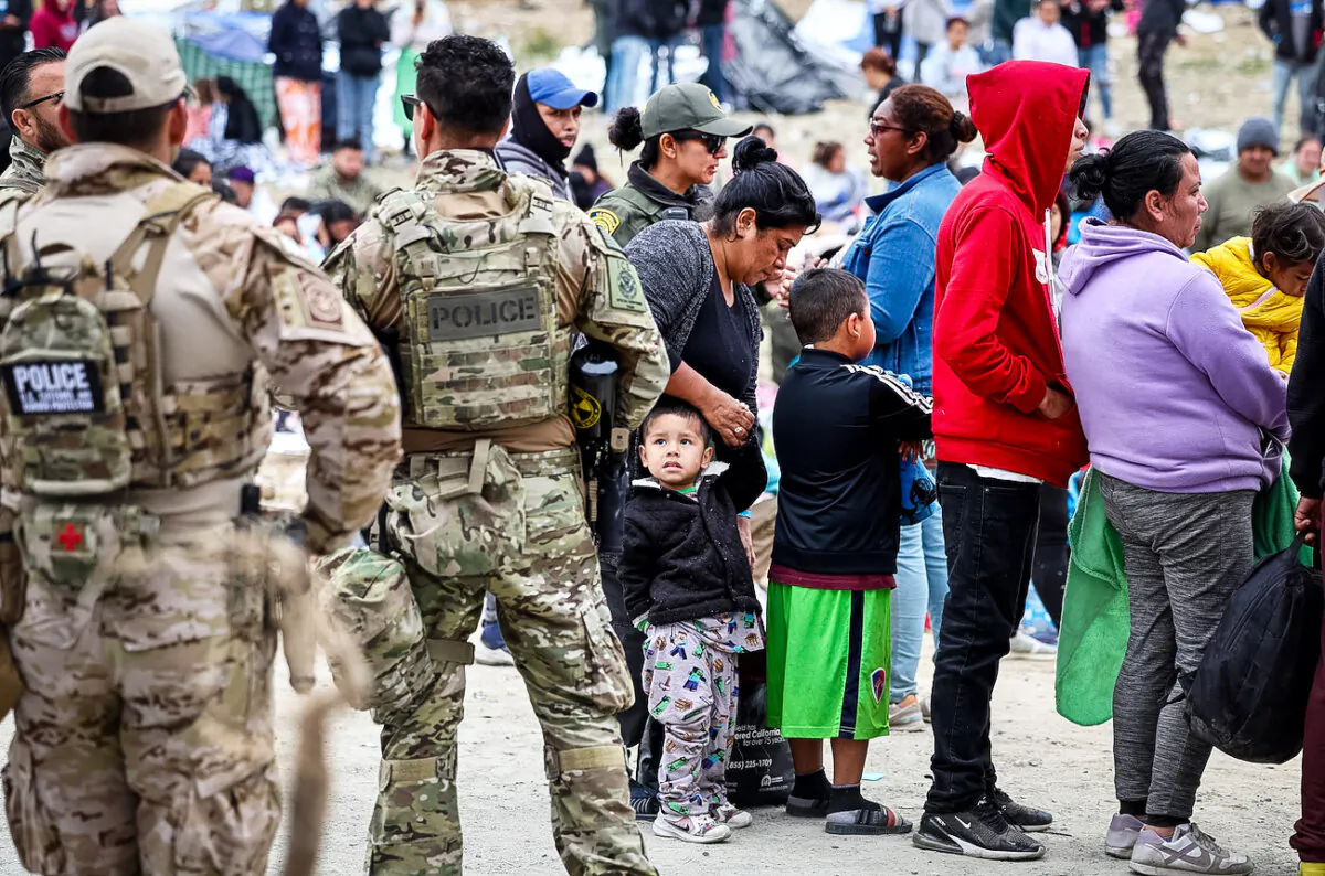 Federal law enforcement agents and officers keep watch as immigrants line up (R) to be transported from a makeshift camp between border walls between the U.S. and Mexico in San Diego, California, on May 13, 2023. (Mario Tama/Getty Images)