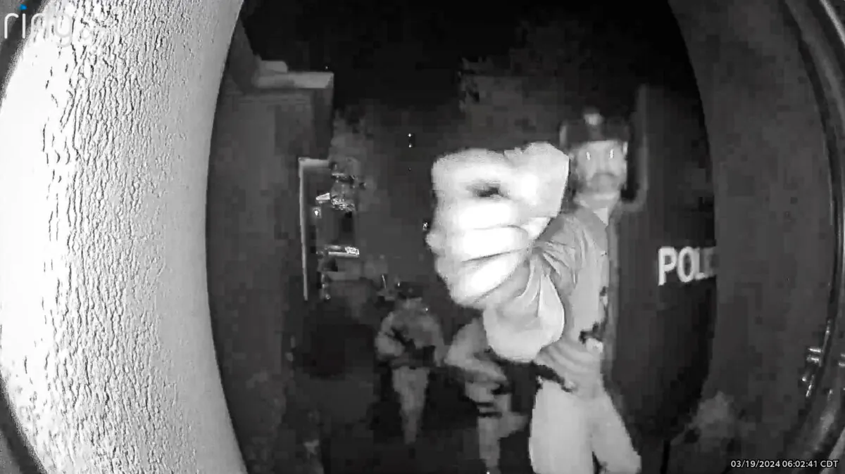 An armed Bureau of Alcohol, Tobacco, Firearms and Explosives agent reaches toward the doorbell camera at the home of Bryan Malinowski moments before disabling the video recording and breaching the door with a tactical team in a predawn raid in West Little Rock, Ark., on March 19, 2024. (Malinowski Family via Bud Cummins)