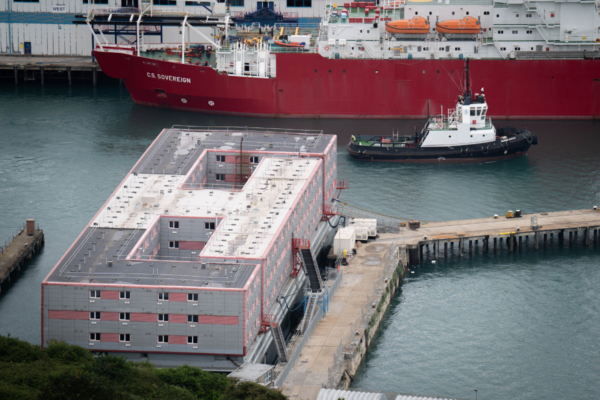 File photo of a tug boat passing the Bibby Stockholm accommodation barge at Portland Port in Dorset, which will house up to 500 people on March 20, 2024. (James Manning/PA Wire)