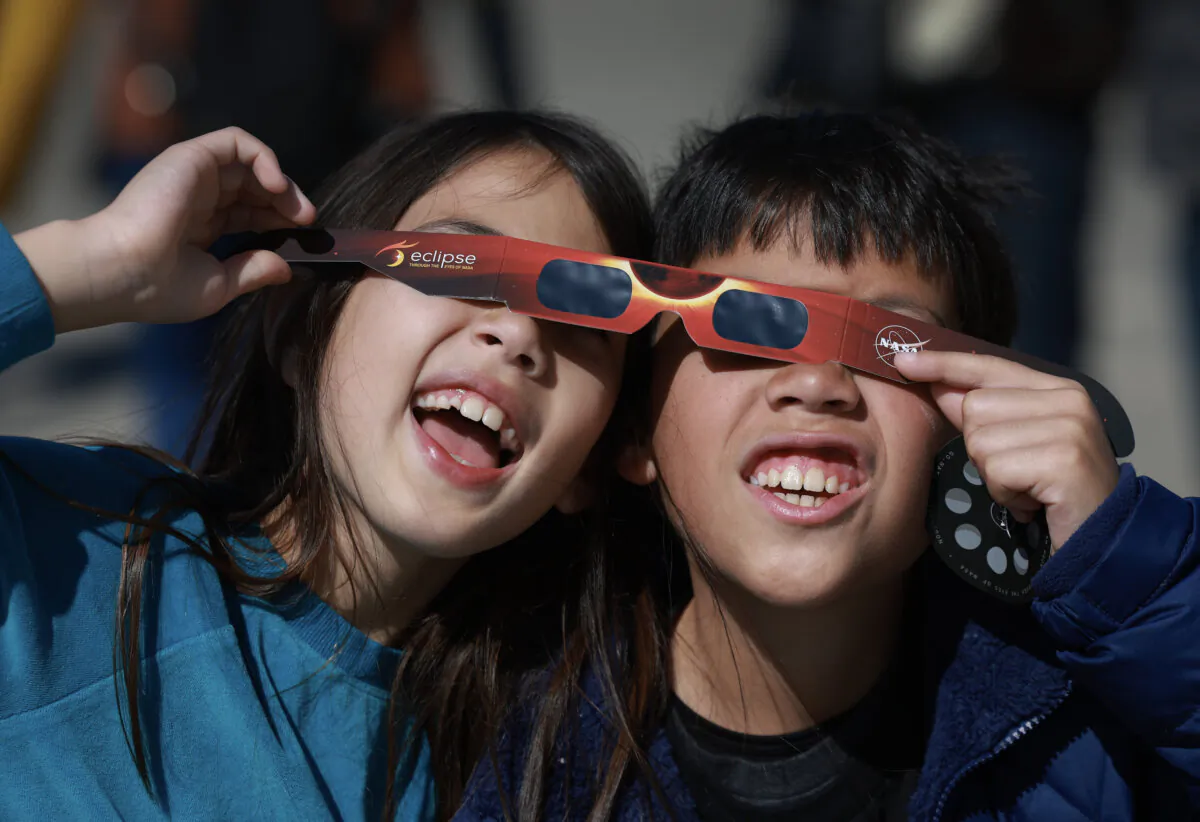 Miriam Toy (L) and Oliver Toy share a pair of eclipse glasses that NASA was handing out as they await the eclipse in Houlton, Maine, on April 8, 2024. (Joe Raedle/Getty Images)