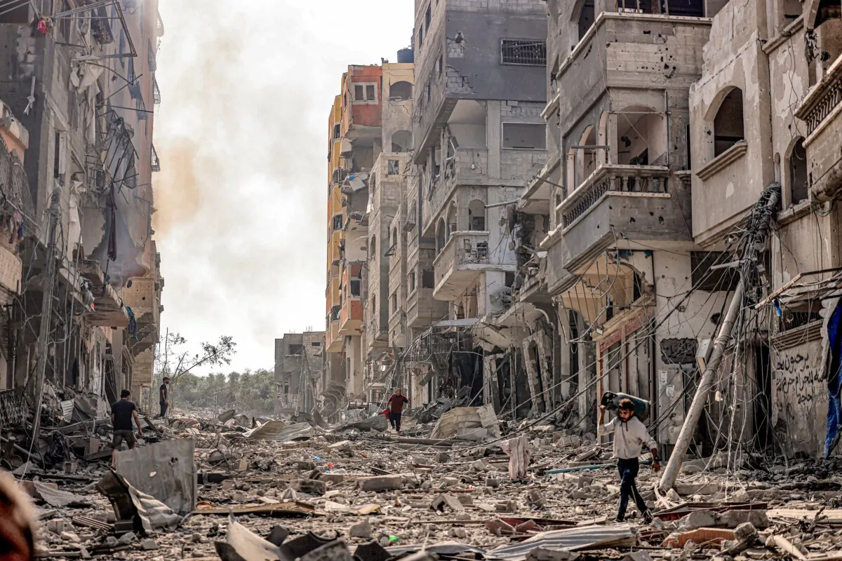 A man carries a propane gas cylinder on his back while walking through debris and destruction littering a street in the Jabalia camp for Palestinian refugees in Gaza City on October 11, 2023, on the fifth day of battles between the Palestinian Islamist movement Hamas and Israel. (Mahmud Hams/AFP via Getty Images)