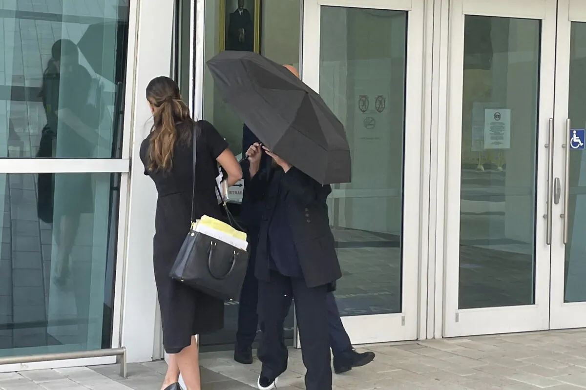 Celebrity handbag designer Nancy Gonzalez hides under an umbrella as she walks with her lawyer Andrea Lopez outside the federal courthouse in Miami on April 22, 2024. (Josh Goodman/AP Photo)