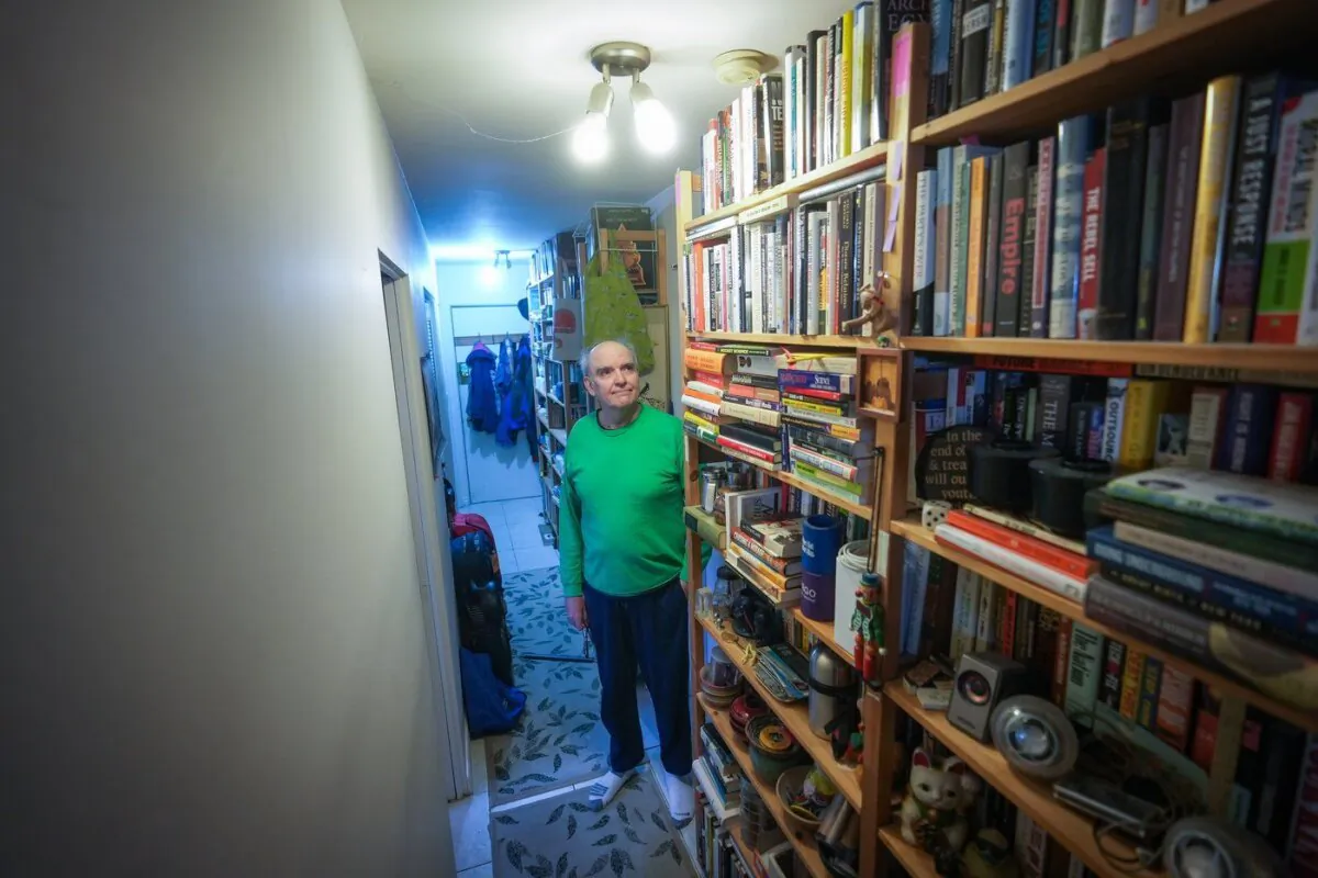 John William, who is losing his sight, poses for a photograph with his collection of books that he has decided to sell, in Vancouver, on Apr. 24, 2024. (The Canadian Press/Darryl Dyck)
