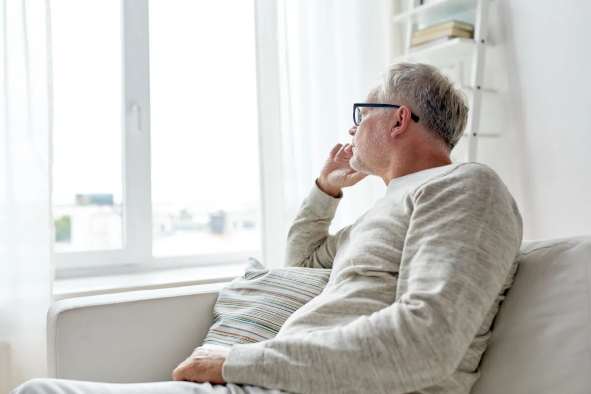 A senior man looks out the window. (Ground Picture/Shutterstock)