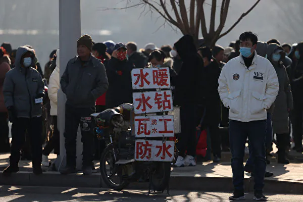 Migrant workers wait for job opportunities on the roadside near signs advertising their skills in Shenyang, Liaoning Province, China on Feb. 6, 2023. (STR / AFP)
