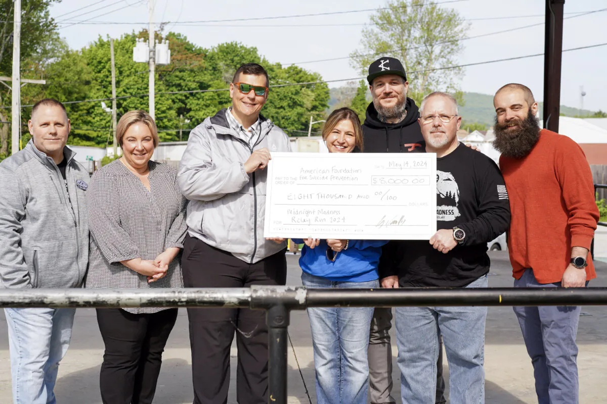 Maria Idoni (C), local director for the American Foundation for Suicide Prevention, receives a check from Midnight Madness relay race organizers and volunteers in Port Jervis, N.Y., on May 14, 2024. (Cara Ding/The Epoch Times)