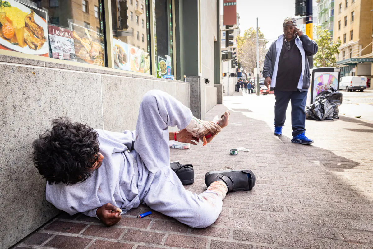 An outreach volunteer checks on the well-being of homeless drug addicts in the Tenderloin District of San Francisco on May 16, 2024. (John Fredricks/The Epoch Times)