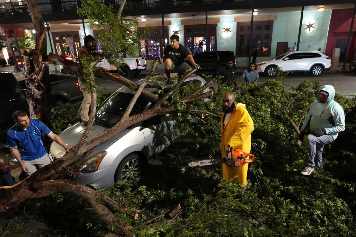 Rapper Trae tha Truth, in yellow, cuts fallen tree limbs on top of a car in the aftermath of a severe thunderstorm that passed through downtown, in Houston on May 16, 2024. (David J. Phillip/AP Photo)