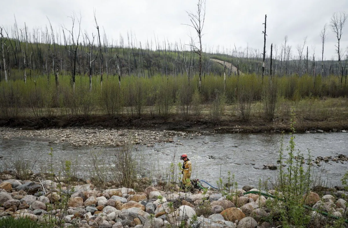 A firefighters monitors a pump in a river bed used for wildfire sprinklers in the evacuated neighbourhood of Grayling Terrace in Fort McMurray, Alta., May 16, 2024. (The Canadian Press/Jeff McIntosh)