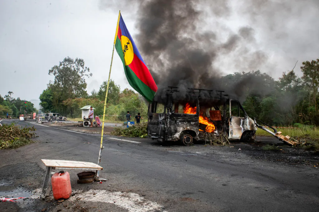 This photograph shows a Kanak flag waving next to a burning vehicle at an independantist roadblock at La Tamoa, in the commune of Paita, France's Pacific territory of New Caledonia on May 19, 2024. (Delphine Mayeur/AFP via Getty Images)
