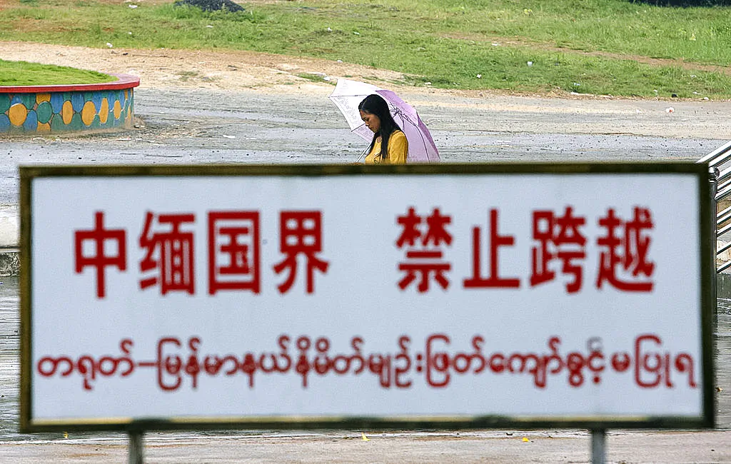 A Burmese woman walks behind a warning sign along the boundary line in the China–Burma border town of Wanding, in southwestern Yunnan Province, China, on Sept. 27 2007. (STR/AFP via Getty Images)