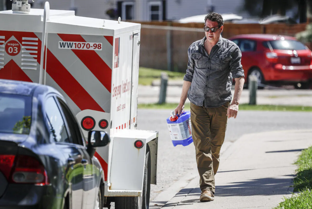 A man leaves with a filled water jug from an emergency supply provided by the city as work to repair a major water main stretches into a second day, in Calgary on June 7, 2024. (The Canadian Press/Jeff McIntosh)
