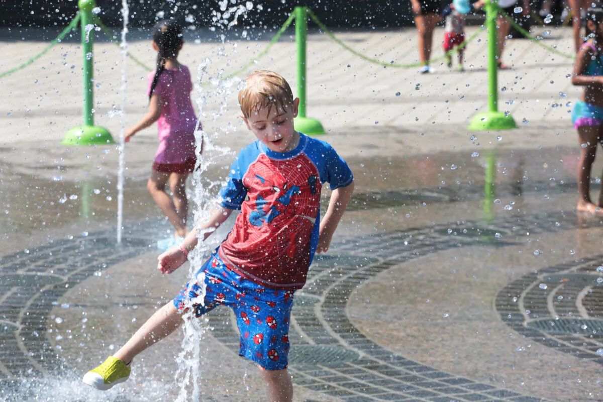 A boy has fun while cooling off at the Pier 84 water fountain in Hell's Kitchen, New York City, on June 19, 2024. (Richard Moore/The Epoch Times)