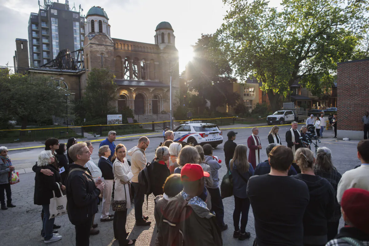 Clergy, parishioners, and community members gather out front of the burnt-out St. Anne's Anglican Church during an evening vigil to mourn the loss of the church, on June 11, 2024. (The Canadian Press/Cole Burston)