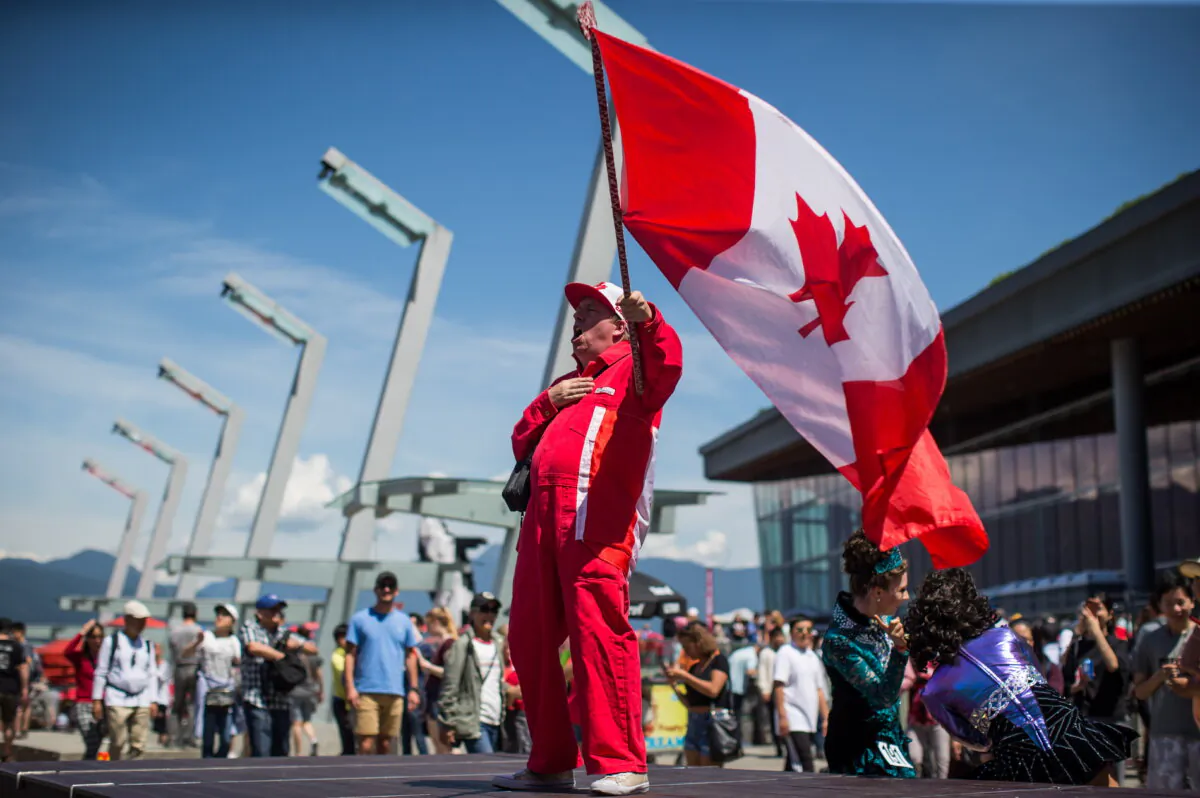 A man waves a Canadian flag on a hockey stick as he sings “O Canada” while attending Canada Day celebrations in Vancouver on July 1, 2019. (The Canadian Press/Darryl Dyck)
