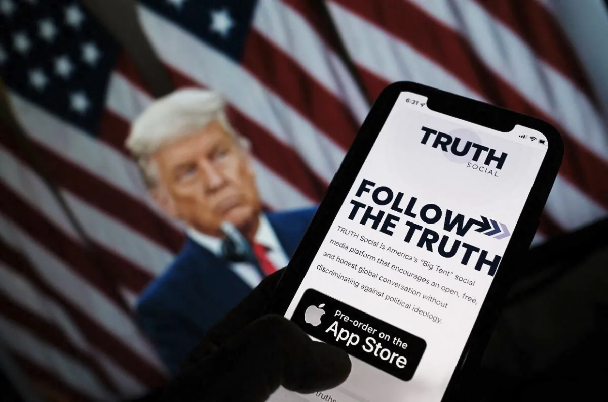 This illustration photo shows a person checking the app store on a smartphone for Truth Social with a photo of former President Donald Trump on a computer screen in the background, in Los Angeles, October 20, 2021. (Chris Delmas/AFP via Getty Images)