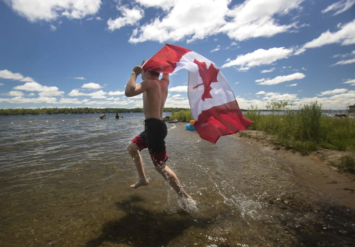 A young boy runs with a Canadian flag at Balsam Lake Provincial Park near Coboconk, Ont., on June 30, 2019. (The Canadian Press/Fred Thornhill)