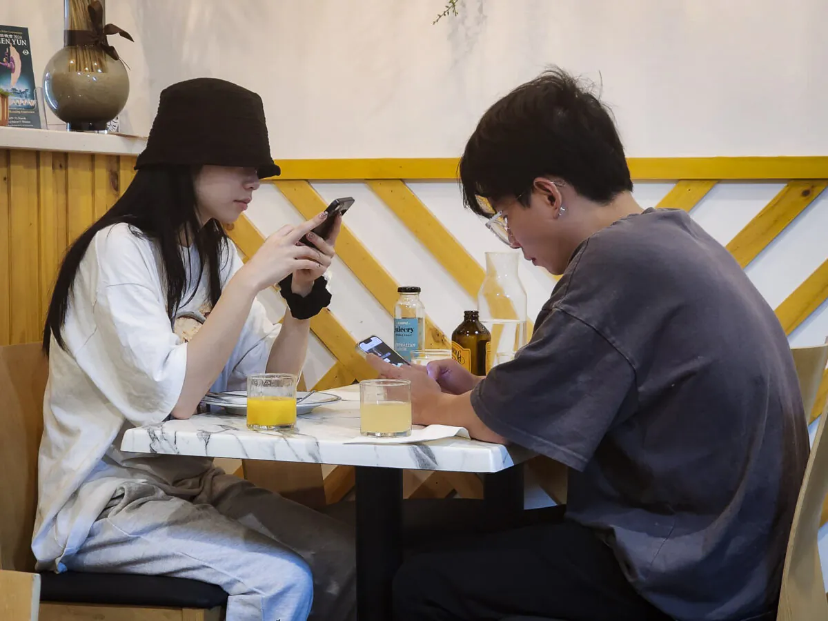 A young couple are absorbed in their mobile phones in Perth, Western Australia, on March 16, 2024. (Susan Mortimer/The Epoch Times)