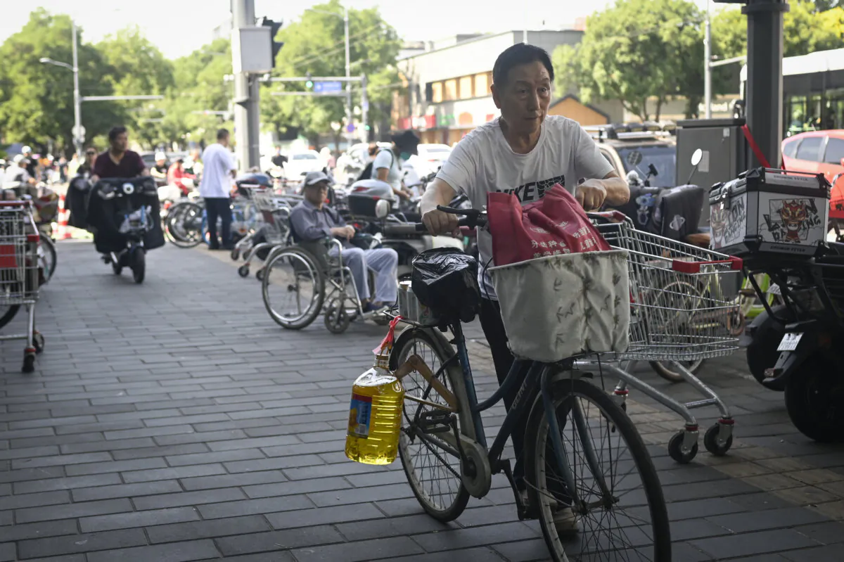 A man riding a bicycle with a barrel of cooking oil leaves a supermarket in Beijing on June 12, 2024. (Wang Zhao/AFP via Getty Images)