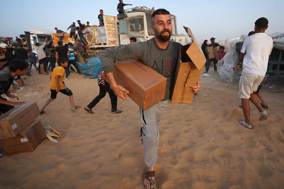 Palestinians carry boxes of humanitarian aid after rushing the trucks transporting the international aid from the US-built Trident Pier near Nuseirat in the central Gaza Strip on May 18, 2024, amid the ongoing conflict between Israel and the militant group Hamas. (AFP via Getty Images)