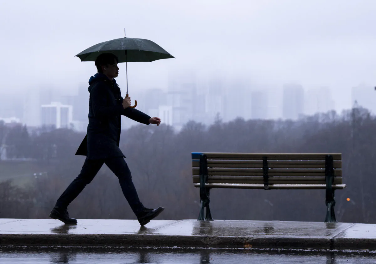 The Toronto skyline is seen shrouded in fog as a man walks in the rain on Dec. 28, 2023. (The Canadian Press/Frank Gunn)
