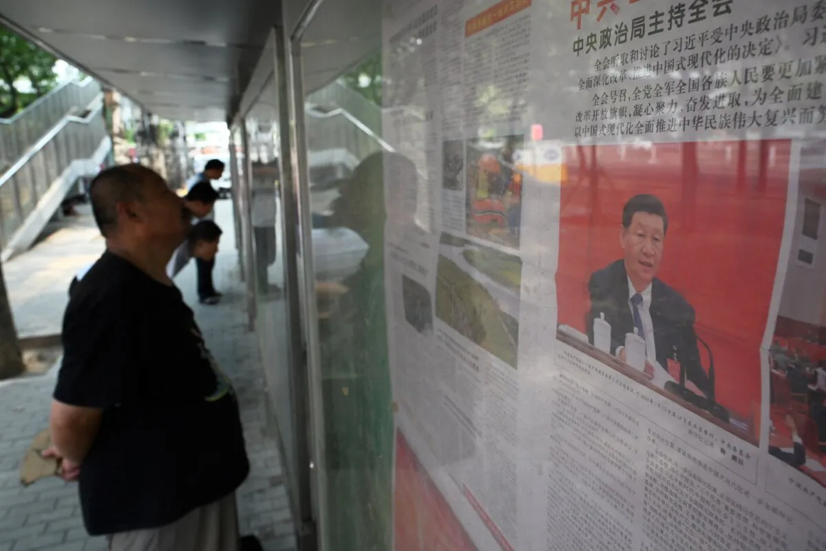 A man reads a newspaper near a front page photo of Chinese leader Xi Jinping on a story about the conclusion of the Third Plenum, a key economic meeting, at a display board on a sidewalk in Beijing on July 19, 2024. (Greg Baker/AFP via Getty Images)