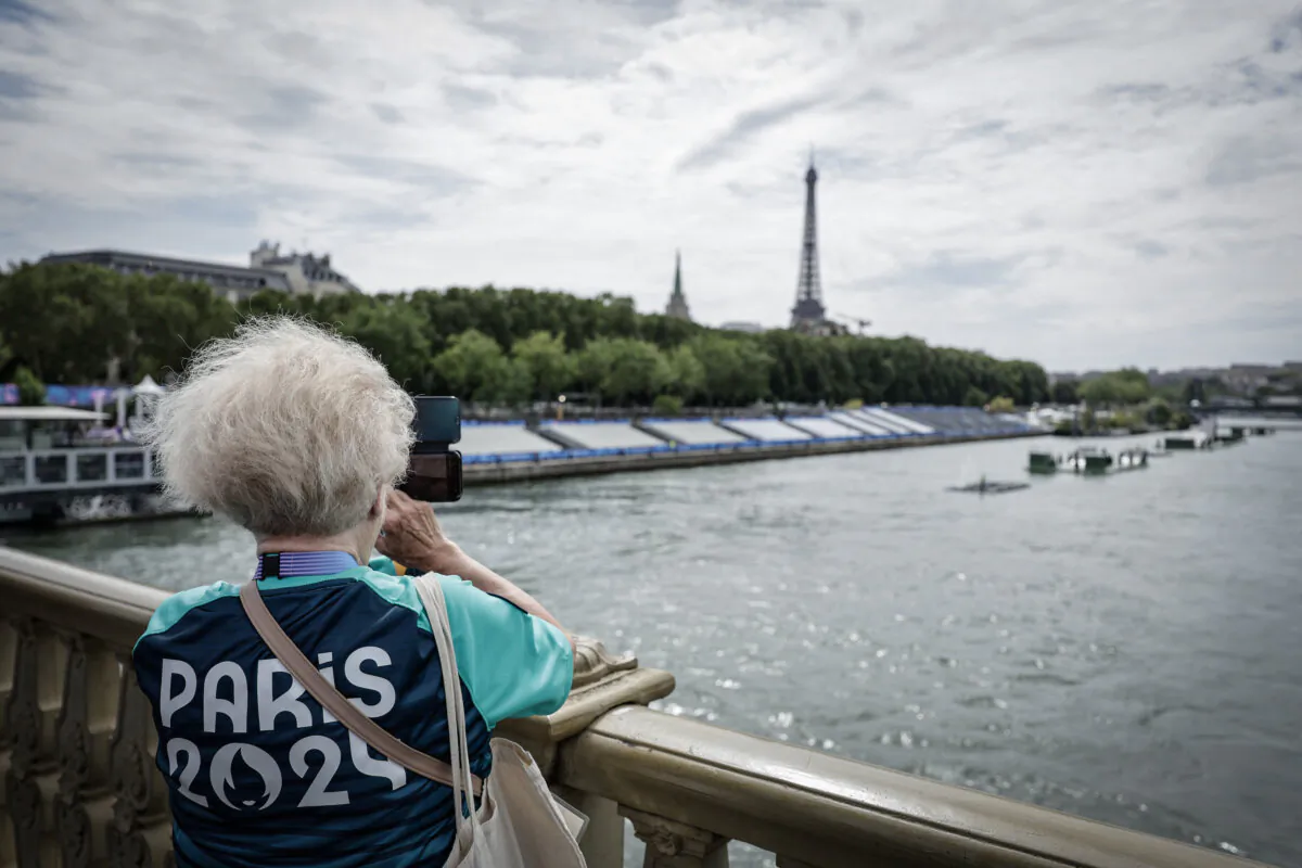 A Paris 2024 volunteer takes a picture on the Invalides bridge next to the tribunes set up on the Seine river on the eve of the Paris 2024 Olympic Games opening ceremony in Paris on July 25, 2024. (Stephane De Sakutin/AFP via Getty Images)