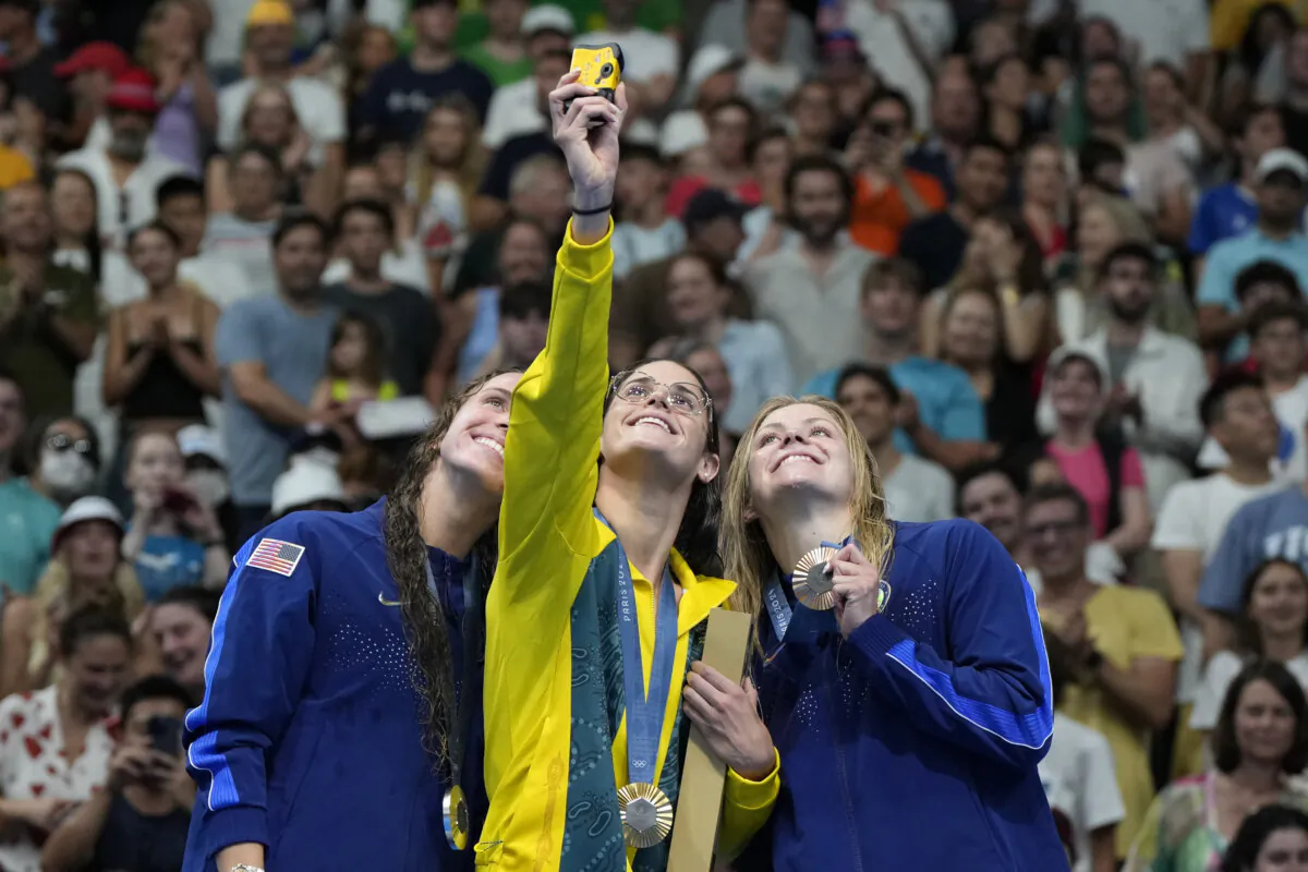 Gold medalist Kaylee McKeown of Australia (C) stands with silver medalist Regan Smith of the United States (L) and bronze medalist Katherine Berkoff of the United States on the podium for a selfie following the women's 100-meter backstroke final at the Olympics in Nanterre, France, on July 30, 2024. (Matthias Schrader/AP Photo)